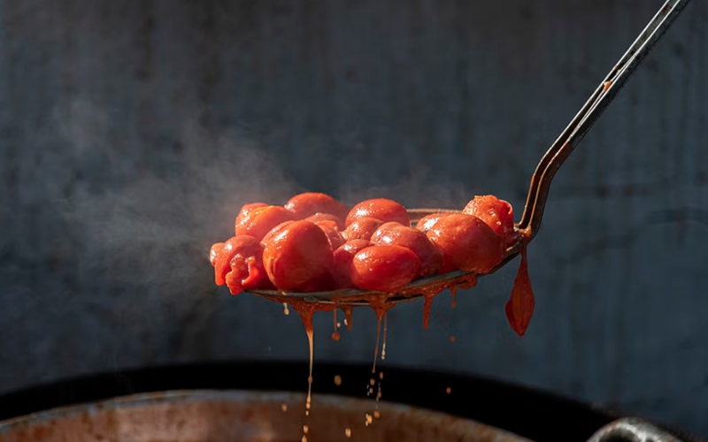 Cherry tomatoes on spoon above pot