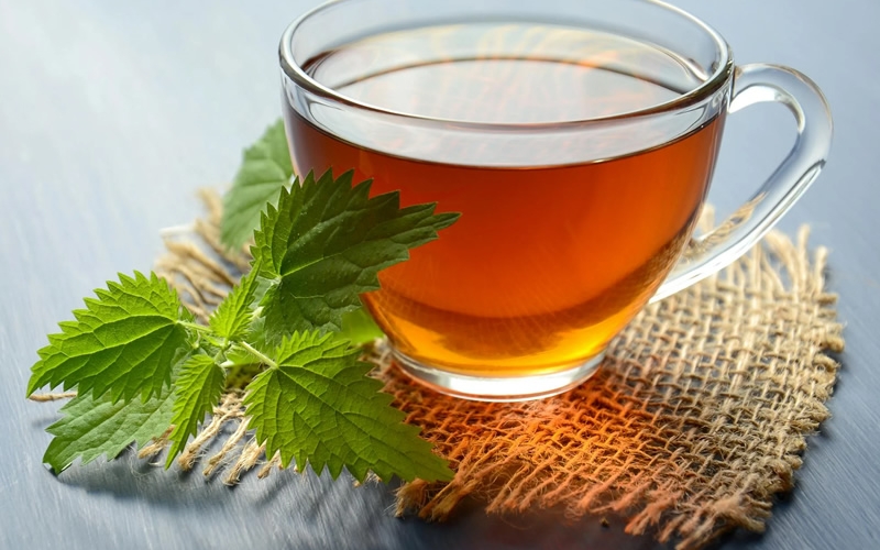 Clear glass teacup with amber tea on a burlap coaster with a green peppermint leaf beside the teacup.