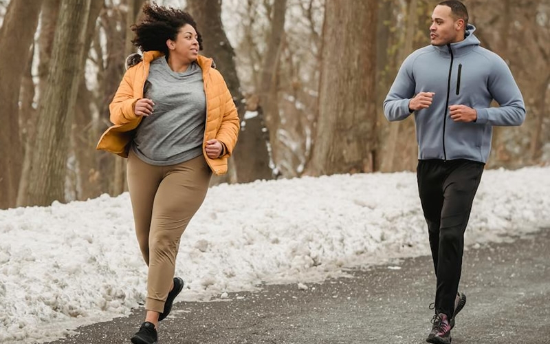 Two people running on a road with snowbanks along the side.