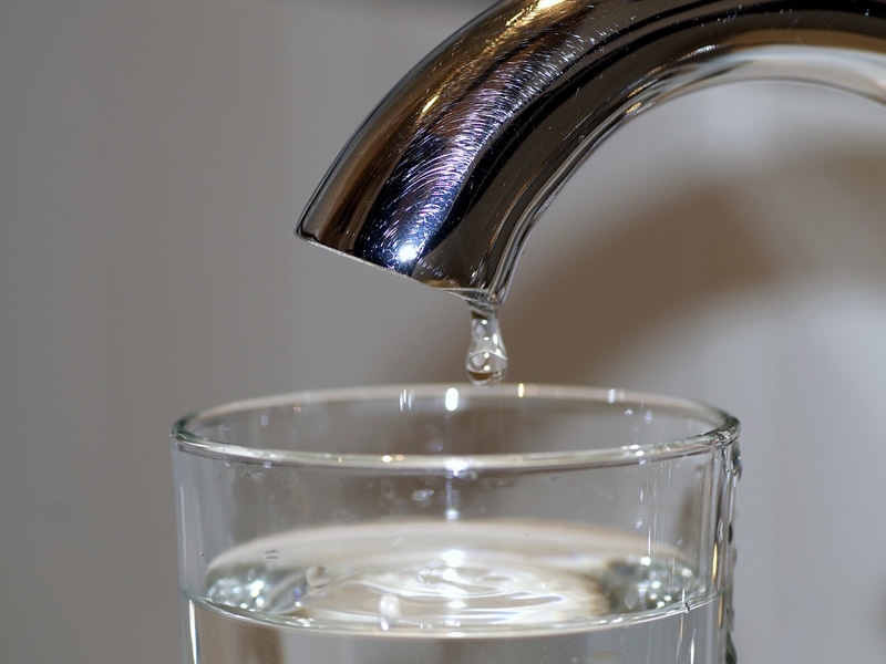 curved water faucet with a drop of water falling into a clear glass