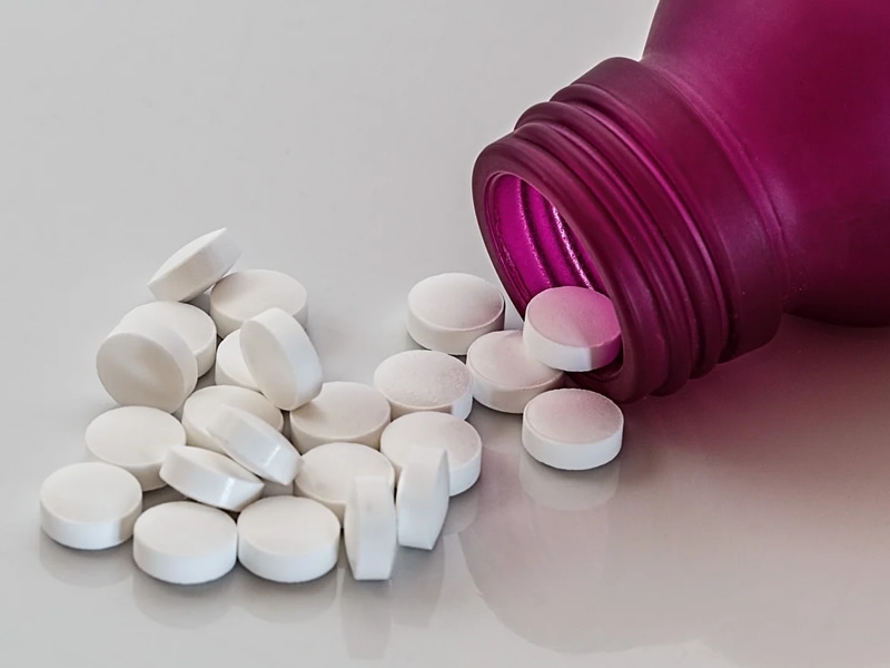 small round white pills spilling out of a purple bottle on a gray countertop