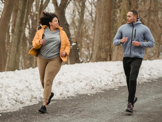 Two people running on a road with snowbanks along the side.